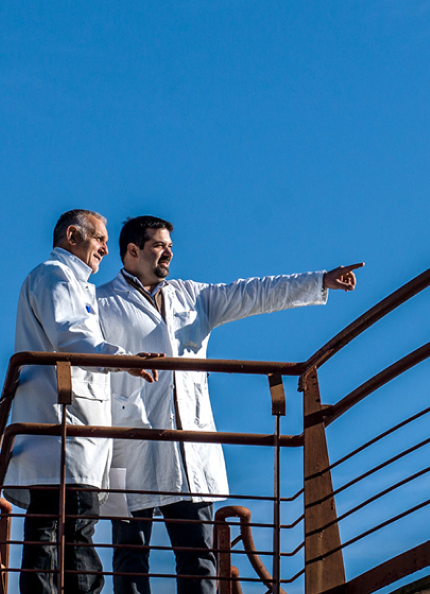 due dipendenti Acea Infrastructure con il camice bianco; uno di loro indica un punto in lontananza. Sullo sfondo un bel cielo sereno