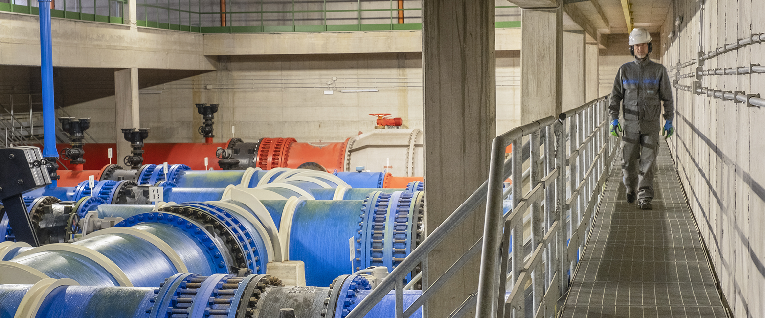 Infrastructure of the water main, with large blue and orange pipes, an iron bridge on which a worker is walking