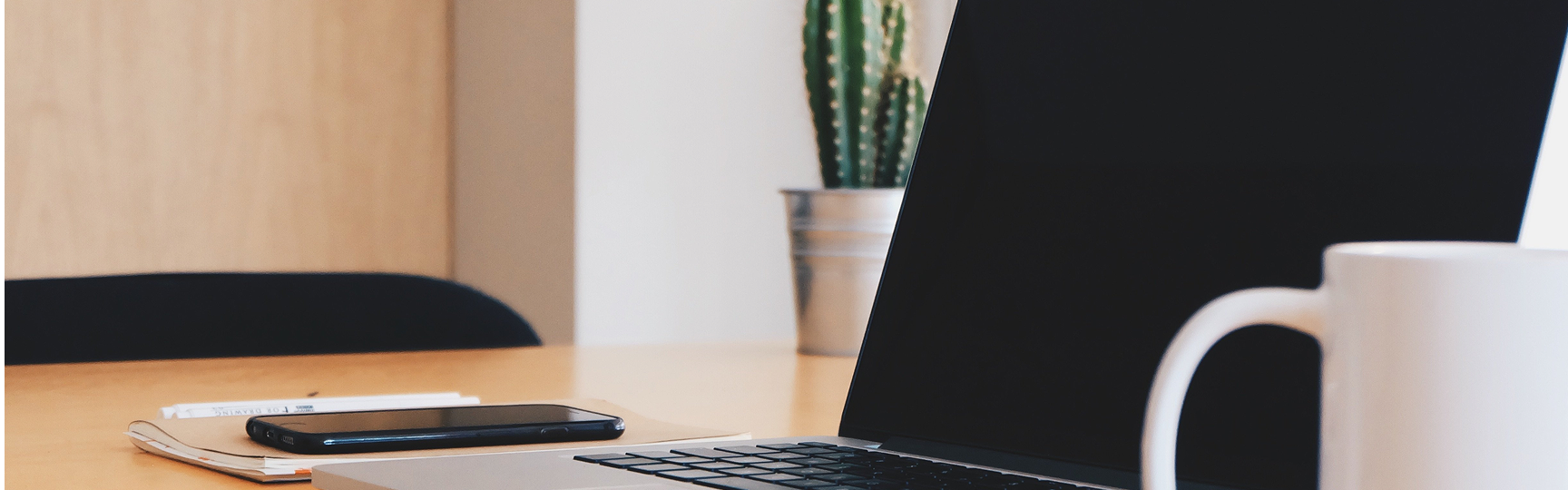 Laptop poggiato su una scrivania d'ufficio. Si vede anche uno smartphone e una pianta di cactus