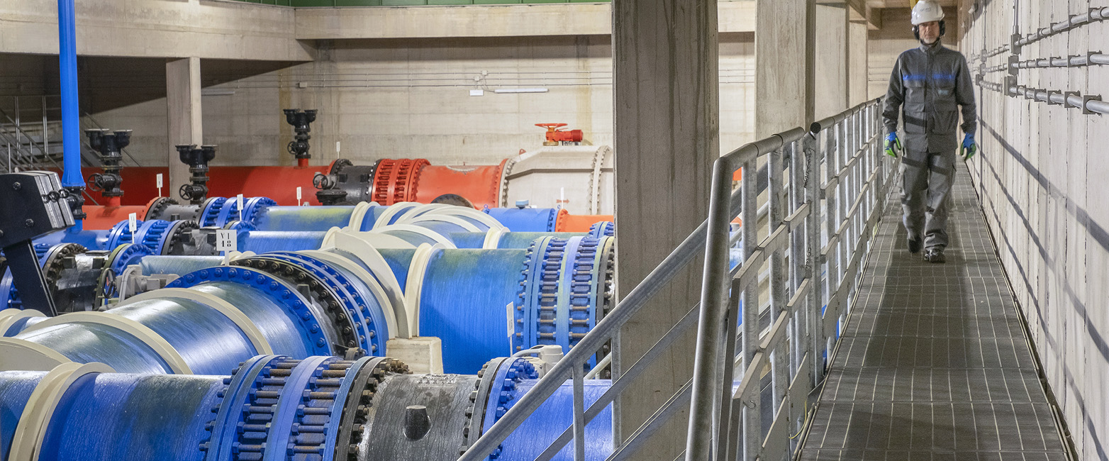 infrastruttura dell'adduttrice, con dei grossi tubi blu e arancioni, un ponte in ferro su cui cammina un operaio