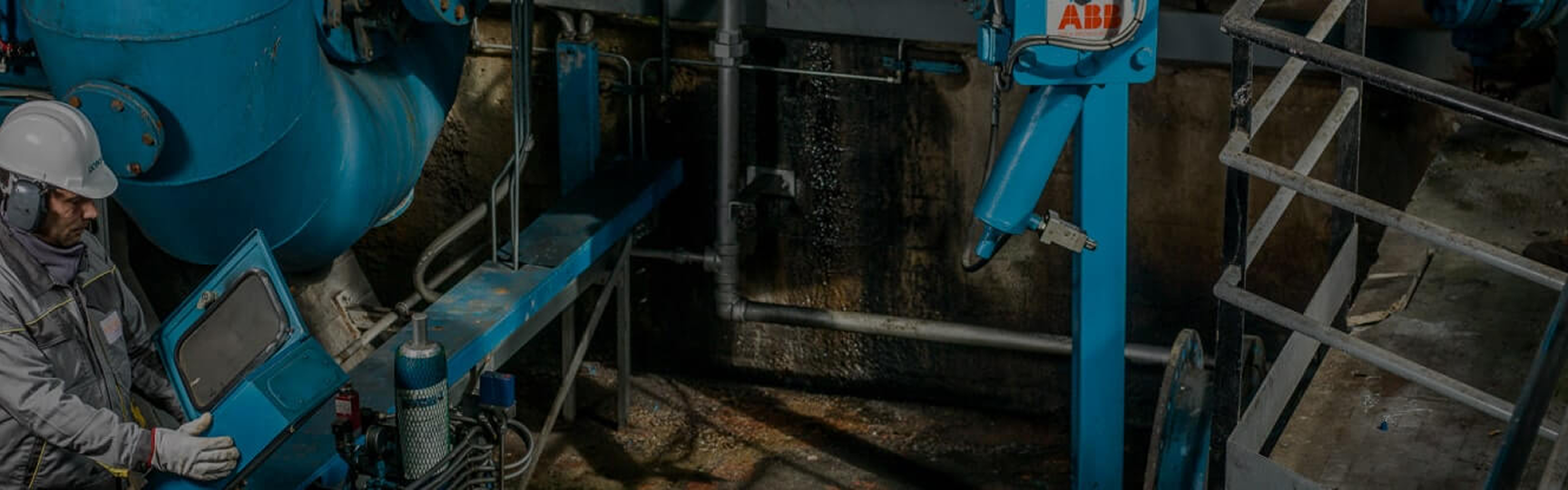 worker testing an electrical cabinet with a large blue pipe in the background
