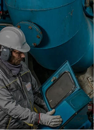worker testing an electrical cabinet with a large blue pipe in the background