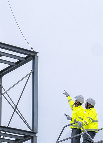Two workers on a structure point out to the tower of the same structure